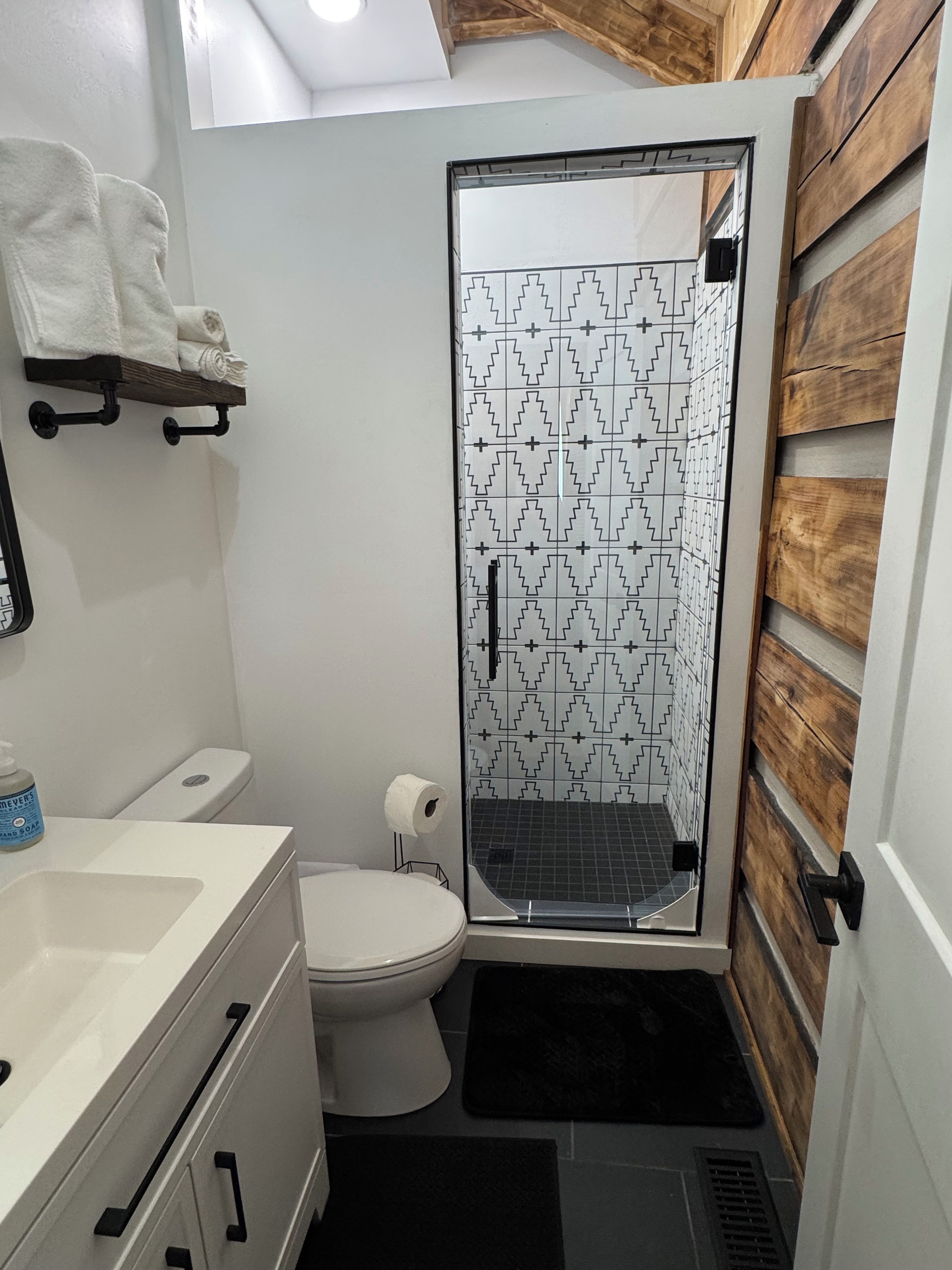 A bathroom with a white toilet, a sink with a mirror, a shower with a patterned glass door, and a towel rack.