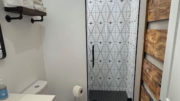 A bathroom with a white toilet, a sink with a mirror, a shower with a patterned glass door, and a towel rack.