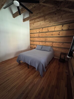 A bedroom with a bed, wooden walls, and a ceiling fan.