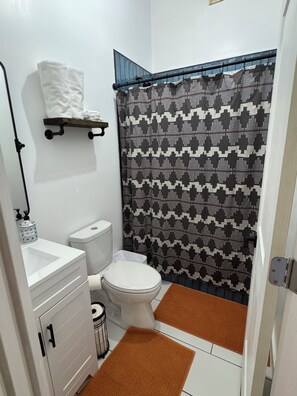 Ein kleines Badezimmer mit Toilette, Waschbecken, Handtuchhalter und Duschvorhang.