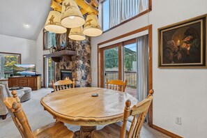 A spacious dining area with a large wooden table and chairs, a stone fireplace, and a scenic view through the glass doors. - Spacious 3 Bedroom, 2 Full Bath with Deck, Private Hot Tub and Mountain Views (Blue River)
