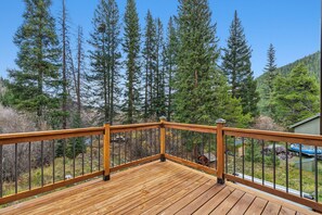 A wooden deck with a metal railing, overlooking a forested area with tall trees. - Spacious 3 Bedroom, 2 Full Bath with Deck, Private Hot Tub and Mountain Views (Blue River)