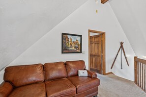 A brown leather sofa in a room with a sloped ceiling, a wooden door, and a painting on the wall. - Spacious 3 Bedroom, 2 Full Bath with Deck, Private Hot Tub and Mountain Views (Blue River)