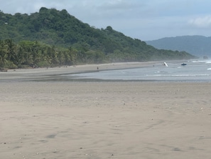 A beach with a sandy shore, a forested hill in the background, and a few people and boats in the water. - New Listing (Santa Teresa)