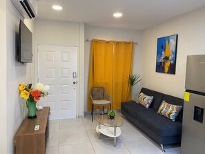 Un salon moderne comprenant un canapé, une table basse, un fauteuil, un téléviseur fixé au mur et une porte.