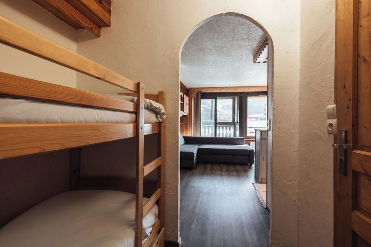 A narrow hallway with bunk beds on one side and a sofa in the other, leading to a room with a window.