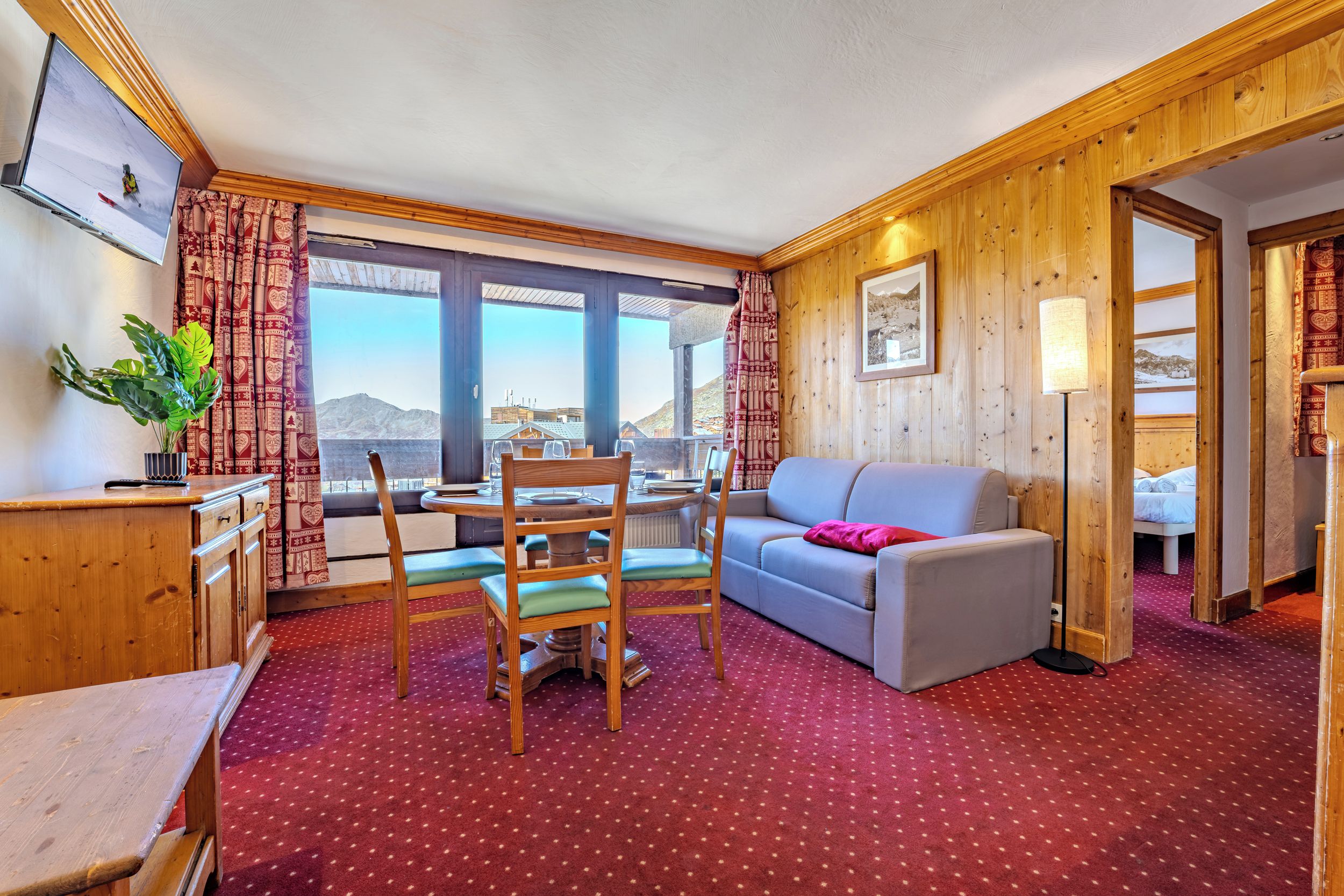 A cozy room with a dining table, chairs, a sofa, and a view of the mountains through large windows.