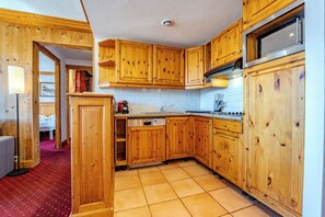 A compact kitchen with wooden cabinets, a built-in dishwasher, and a stainless steel refrigerator. - Glaciers (Les Belleville)