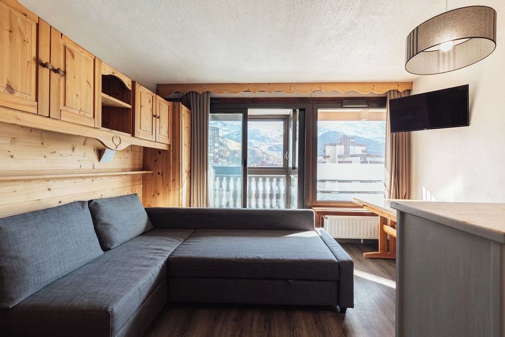 Ein Zimmer mit einer Couch, Holzschränken, einem Fernseher und Blick auf Berge.