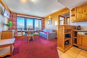 A cozy room with a dining table, chairs, a sofa, and a kitchen area with wooden cabinets and a stove. - Glaciers (Les Belleville)