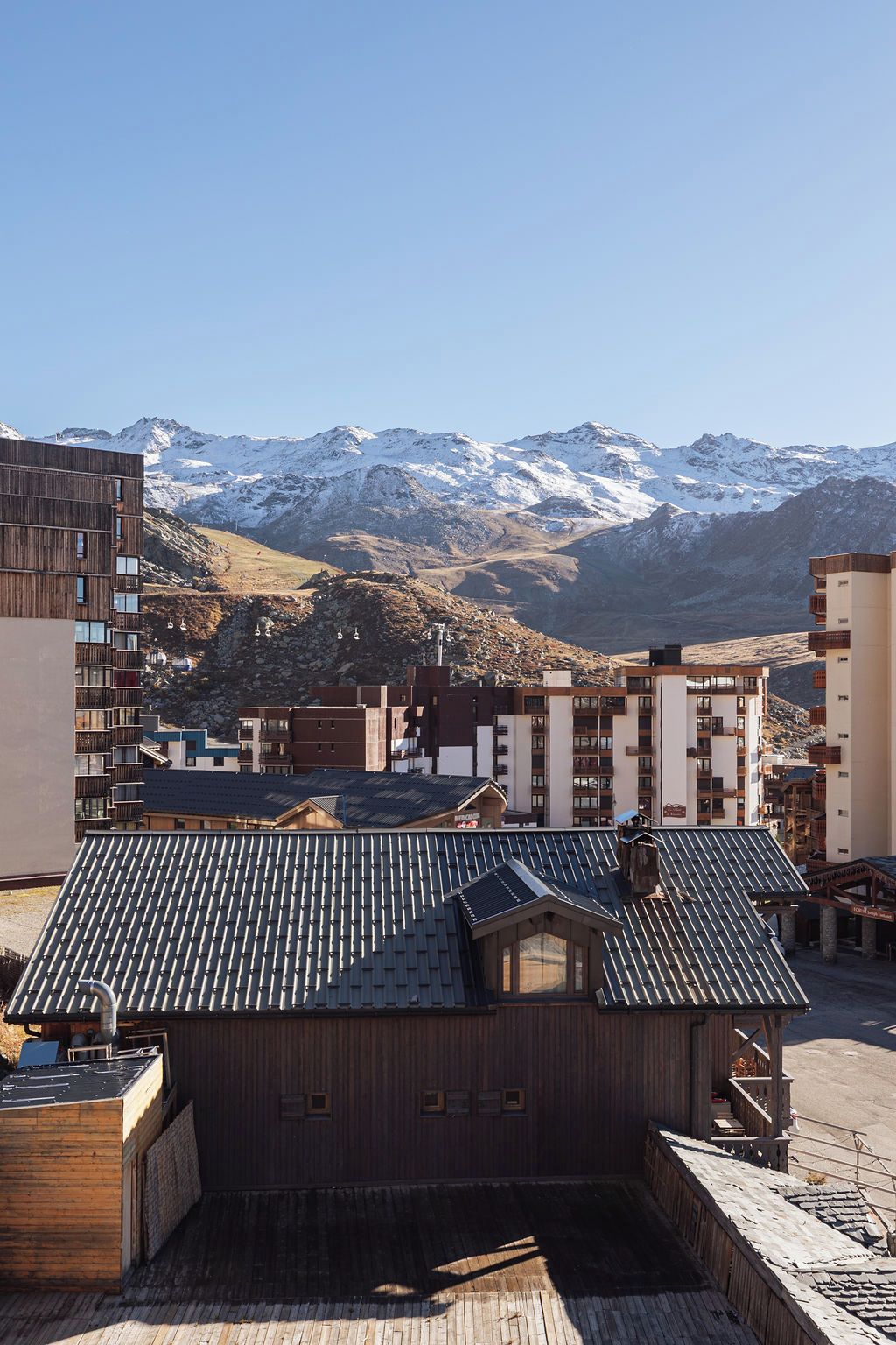 A building with a sloped roof, surrounded by other structures and a mountainous backdrop.