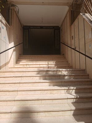 A set of stone steps leading to a dark interior space, with metal railings on either side.