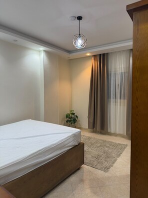 Een slaapkamer met een bed, een kamerplant en uitzicht buiten door een raam met gordijnen.