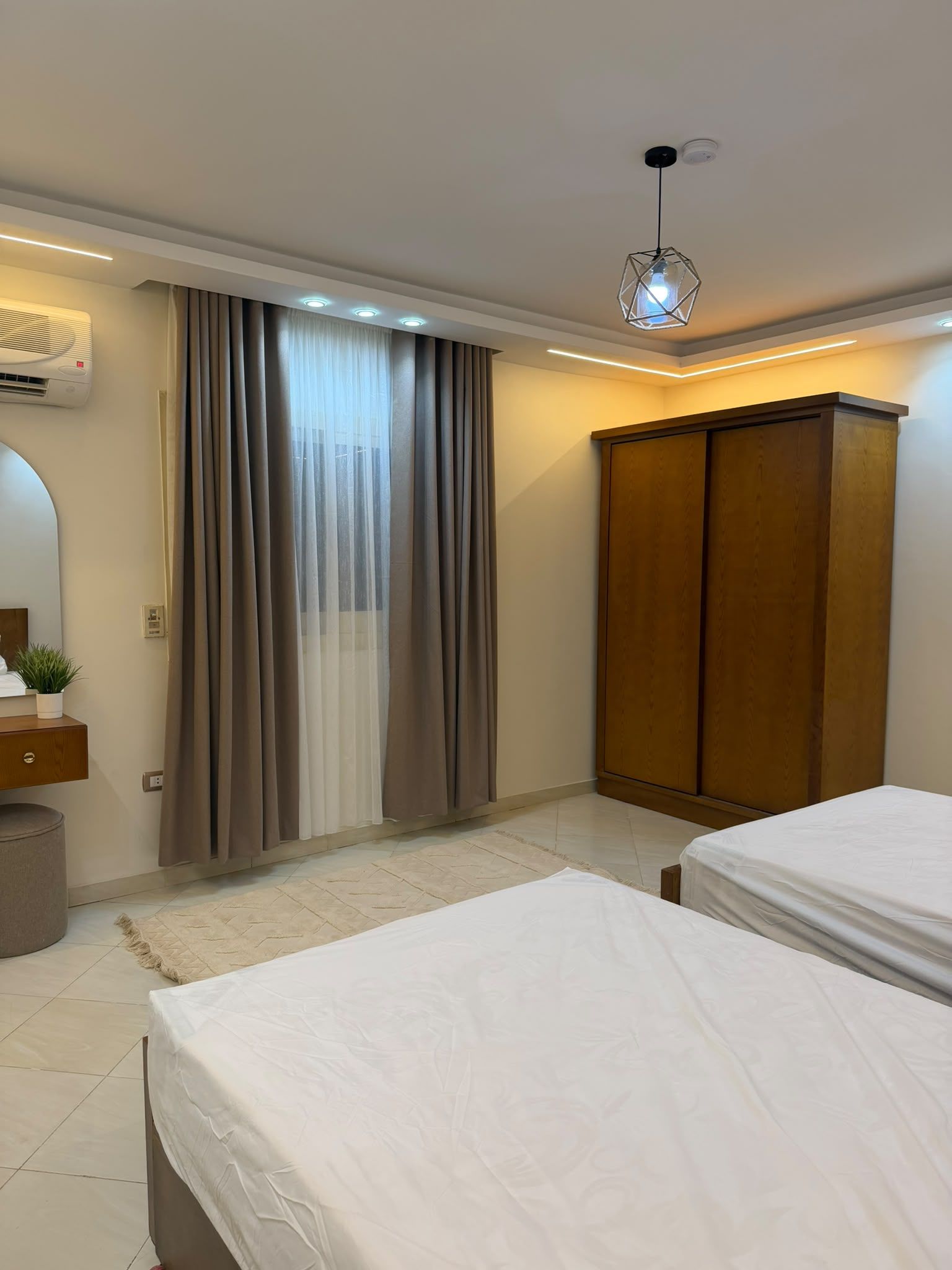 A bedroom with two beds, a wardrobe, a mirror, and an air conditioning unit.