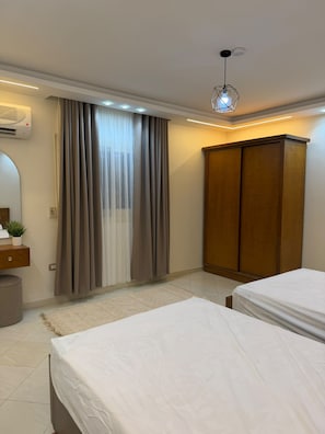 A bedroom with two beds, a wardrobe, a mirror, and an air conditioning unit.