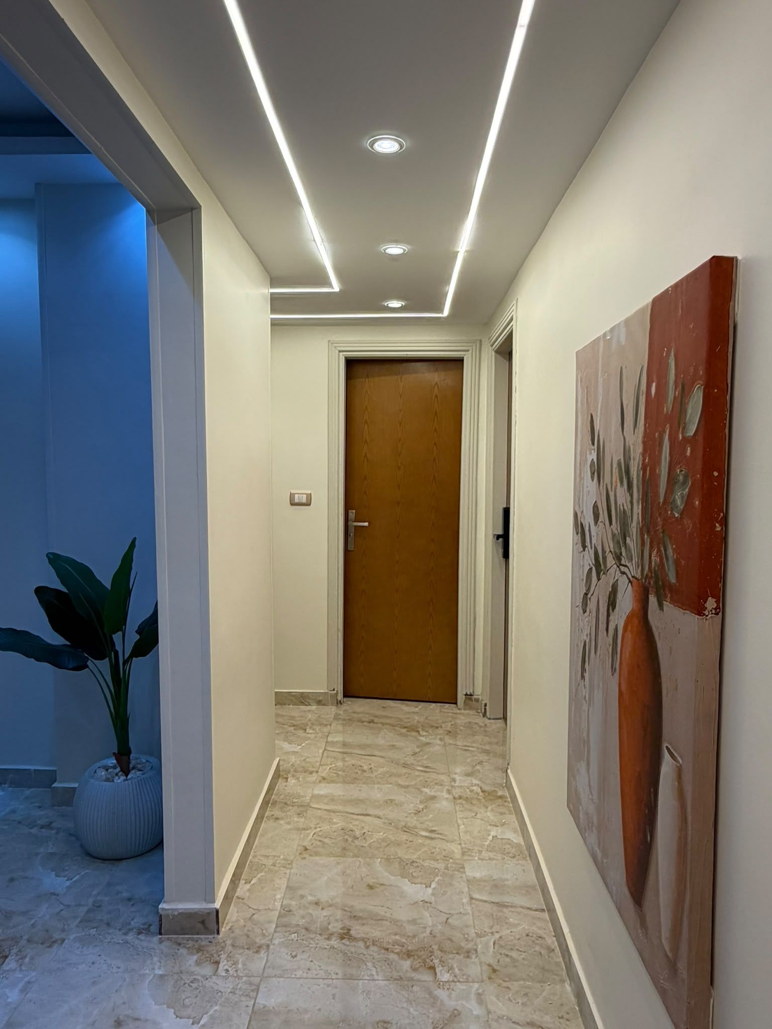 A hallway with a marble floor, a wooden door, and a painting on the wall.