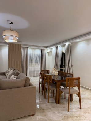A modern living room with a sofa, dining table, and chairs. - Mirage des Pyramides – 3-Bedroom Apartment with Pyramid Views Near GEM (Giza Governorate)
