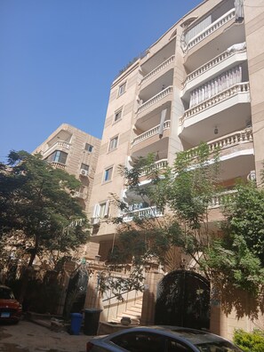A multi-story residential building with balconies, a gated entrance, and a parked car. - Mirage des Pyramides – 3-Bedroom Apartment with Pyramid Views Near GEM (Giza Governorate)