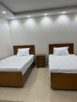 A hotel room with two beds, a small wooden nightstand, and a tiled floor.