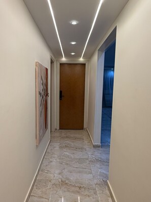 A hallway with a marble floor, a wooden door, and a painting on the wall. - Mirage des Pyramides – 3-Bedroom Apartment with Pyramid Views Near GEM (Giza Governorate)