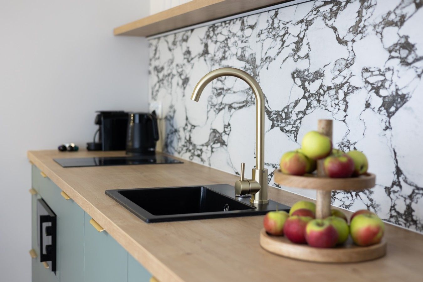 A kitchen with a marble backsplash, a sink with a gold faucet, and a wooden fruit stand.