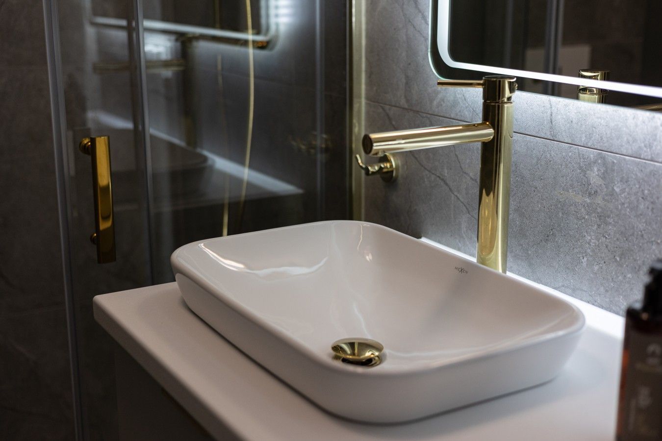 A bathroom with a white sink, a glass shower enclosure, and a gold faucet.