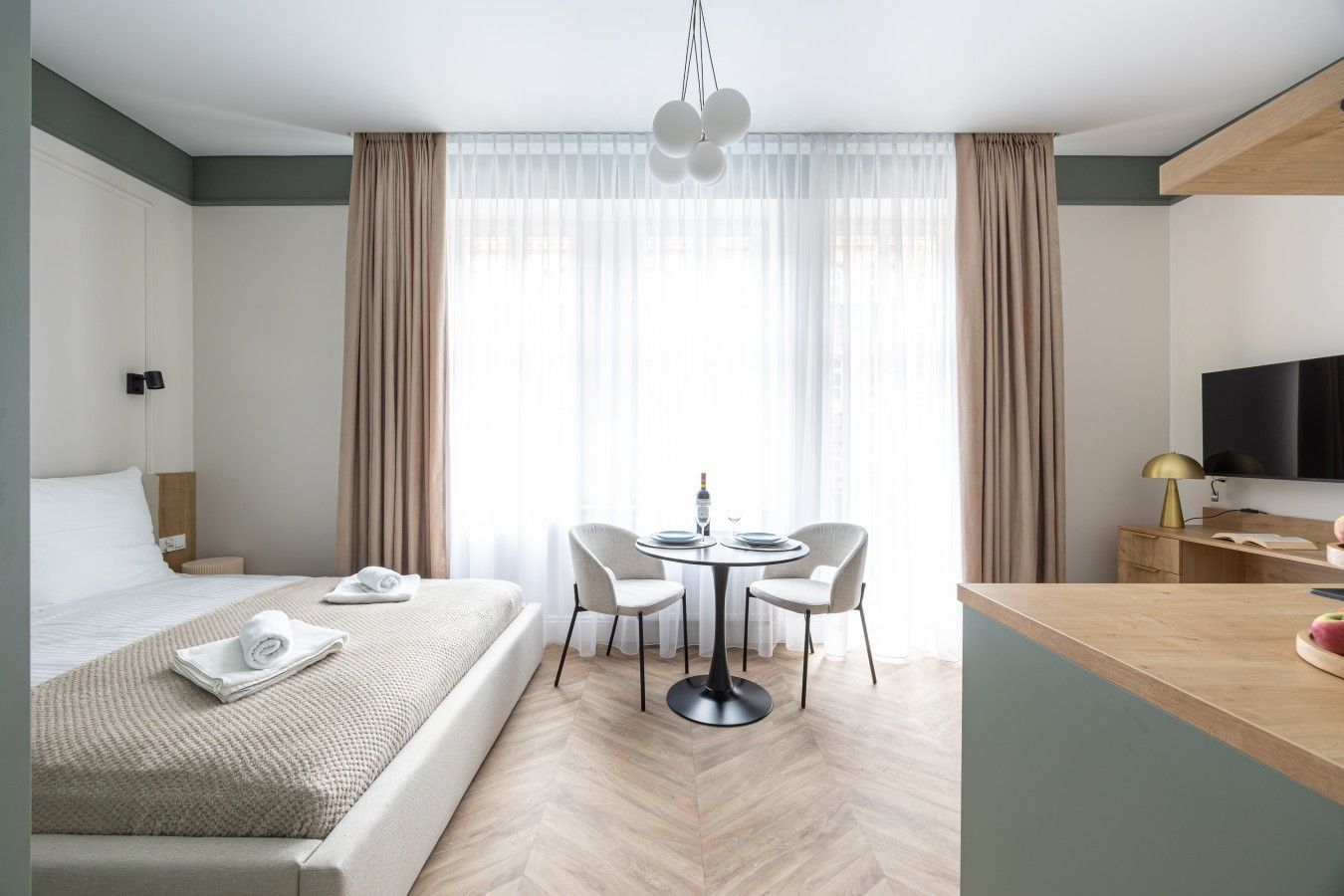 Una habitación de hotel con cama, una mesa de comedor con sillas, un televisor y un escritorio con lámpara.