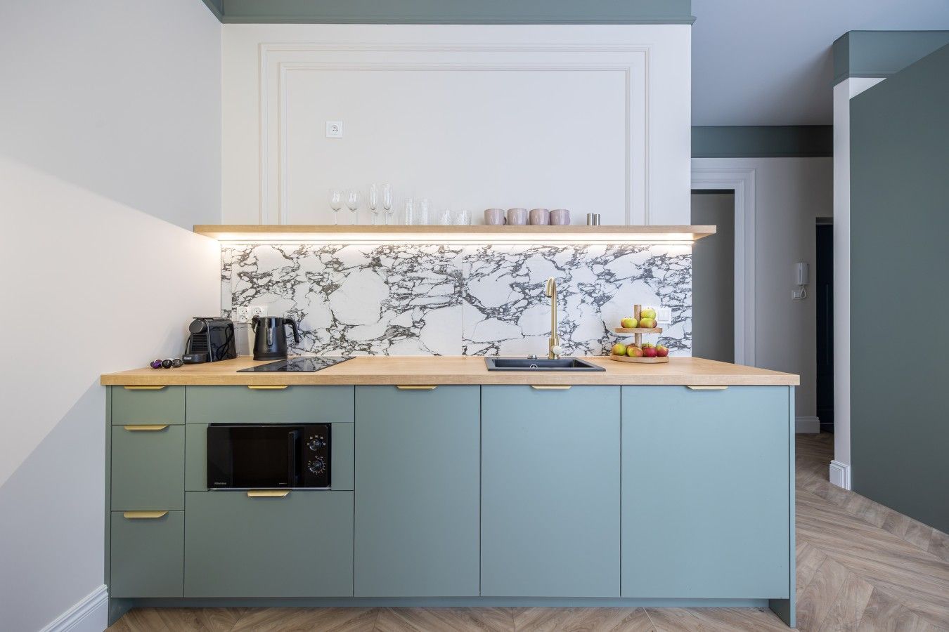 A kitchen with a marble backsplash, a coffee machine, a kettle, and a fruit display.