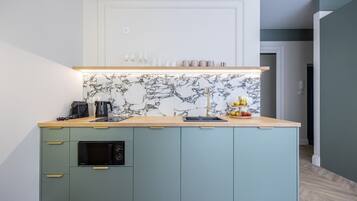 A kitchen with a marble backsplash, a coffee machine, a kettle, and a fruit display.