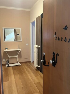 Habitació amb terra de fusta, radiador blanc, una porta decorada amb un gat negre i un mirall a la paret.