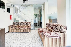 Un vestíbulo con mostrador de recepción, dos sofás estampados, un extintor, una escalera y una puerta de vidrio que da a otra zona.