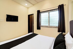 Habitación de hotel con cama, televisor de pantalla plana en la pared, ventana con cortinas y una puerta.