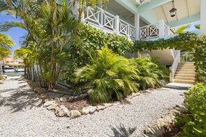 Un edificio con fachada blanca, una escalera y un sendero de grava rodeado de plantas tropicales.