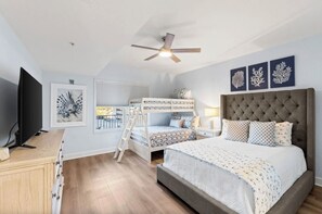 A bedroom with a bunk bed, a large bed, a ceiling fan, and artwork on the wall. - New Rental ~ Book Spring/Summer 2027! (Panama City Beach)