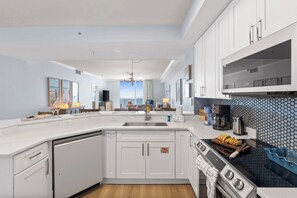 A modern kitchen with white cabinetry, a central island, a stove, and a view to the outside. - New Rental ~ Book Spring/Summer 2027! (Panama City Beach)