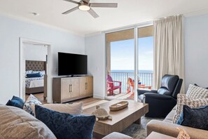 A modern living room with a flat-screen TV, a sofa, a coffee table, and a balcony with a view of the sea. - New Rental ~ Book Spring/Summer 2027! (Panama City Beach)