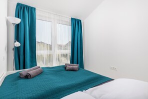 Een hotelkamer met een bed, blauwgroene gordijnen, een raam en een lamp.