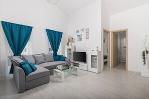 A modern living room with a grey sofa, teal curtains, a glass coffee table, and a TV. - New Listing (Čižići)