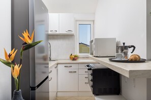 A modern kitchen with white cabinets, a built-in oven, a coffee machine, and a fruit bowl on the counter. - New Listing (Čižići)