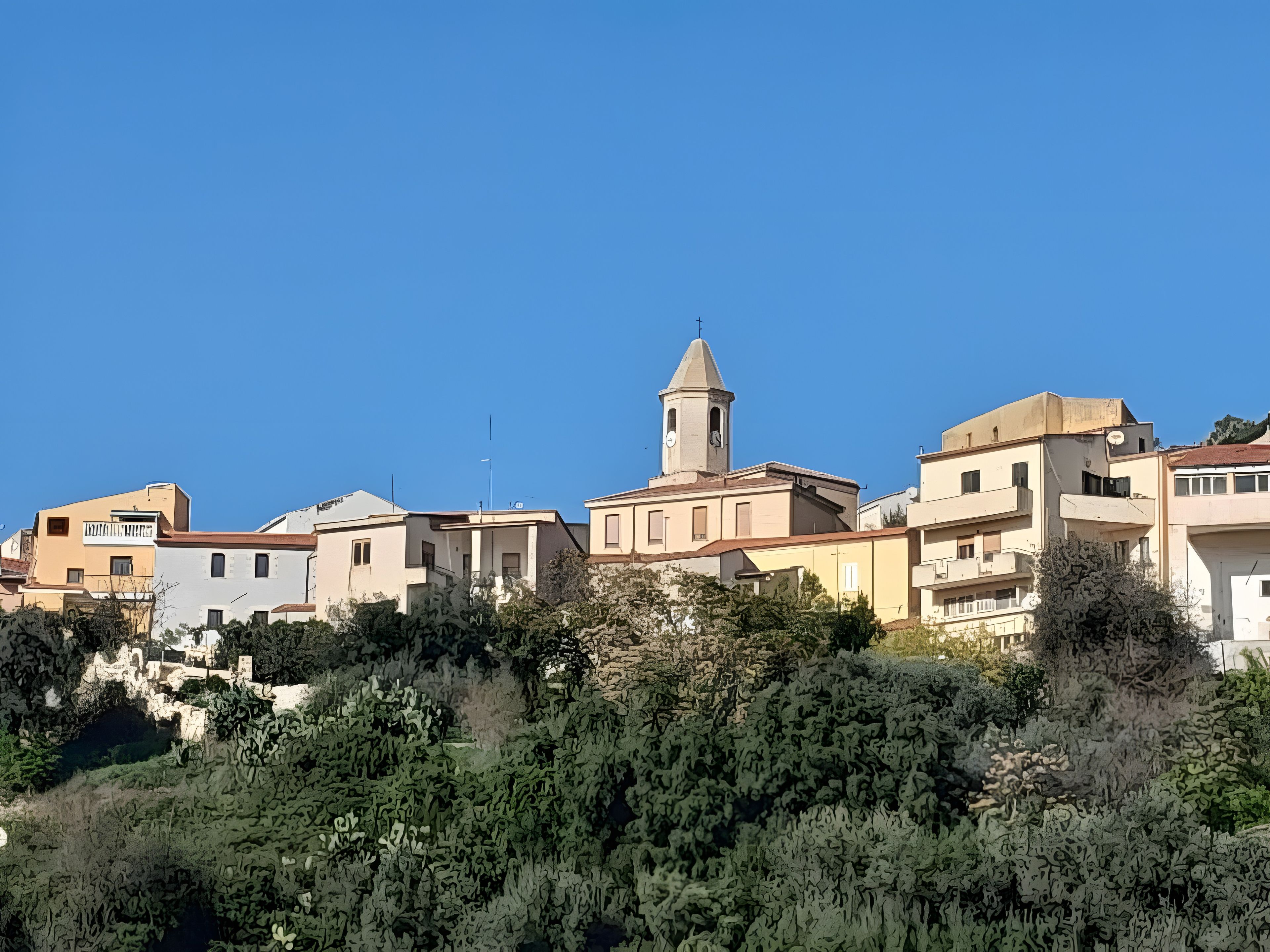 Un pueblo costero con edificios, una torre destacada y abundante vegetación.