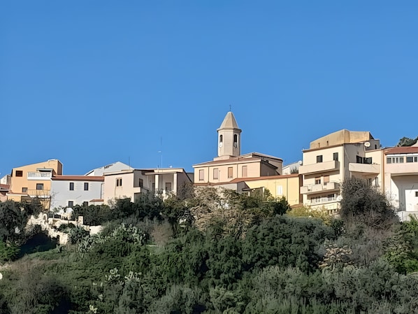 Un pueblo costero con edificios, una torre destacada y abundante vegetación.