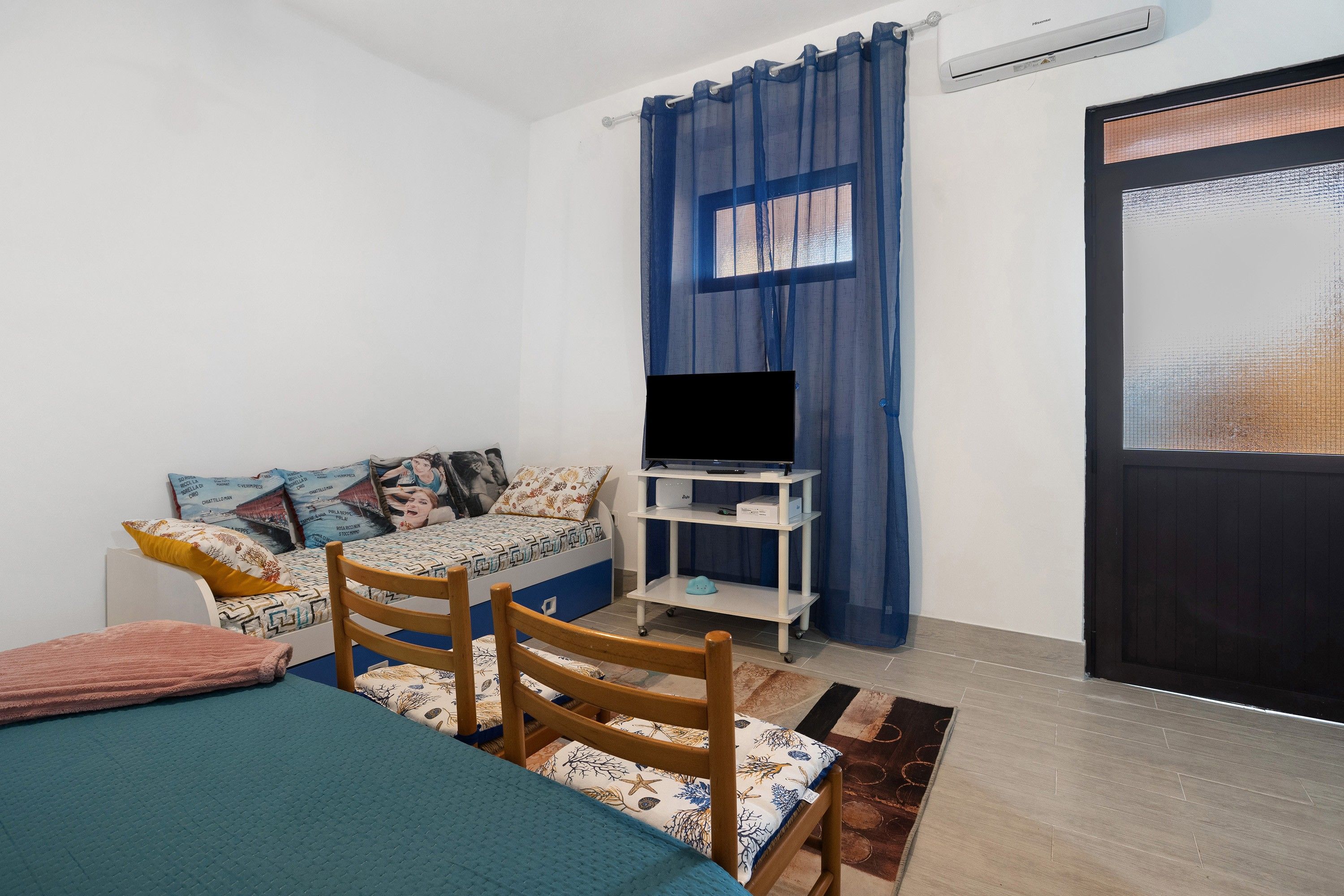 A bedroom with a bed, a desk with a computer, a TV, and a window with curtains.