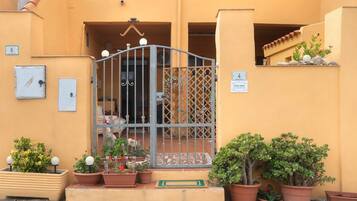 Entrada de um edifício com portão de metal, plantas em vasos e uma placa indicando 'CASA NINA'.
