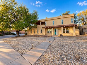 A two-story house with a stone facade, a front porch, and a gravel driveway. - Viva La Vida- Tropical Hacienda + Private Pool (El Paso)