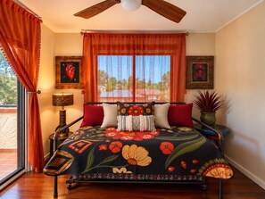 Quarto com cama, cortinas, janela, ventilador de teto e mesa de cabeceira com abajur.