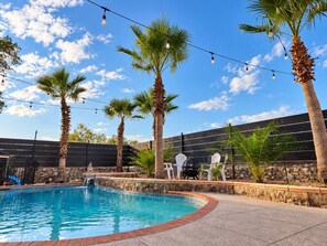 Una piscina con palmeras, un muro de piedra y mobiliario exterior.