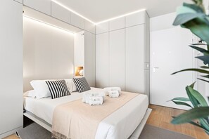 A modern bedroom with a bed, bedside tables, a nightstand, a wardrobe, and a plant. - GuestReady - Modern Studio with Balcony & Pool (Vila Nova de Gaia)