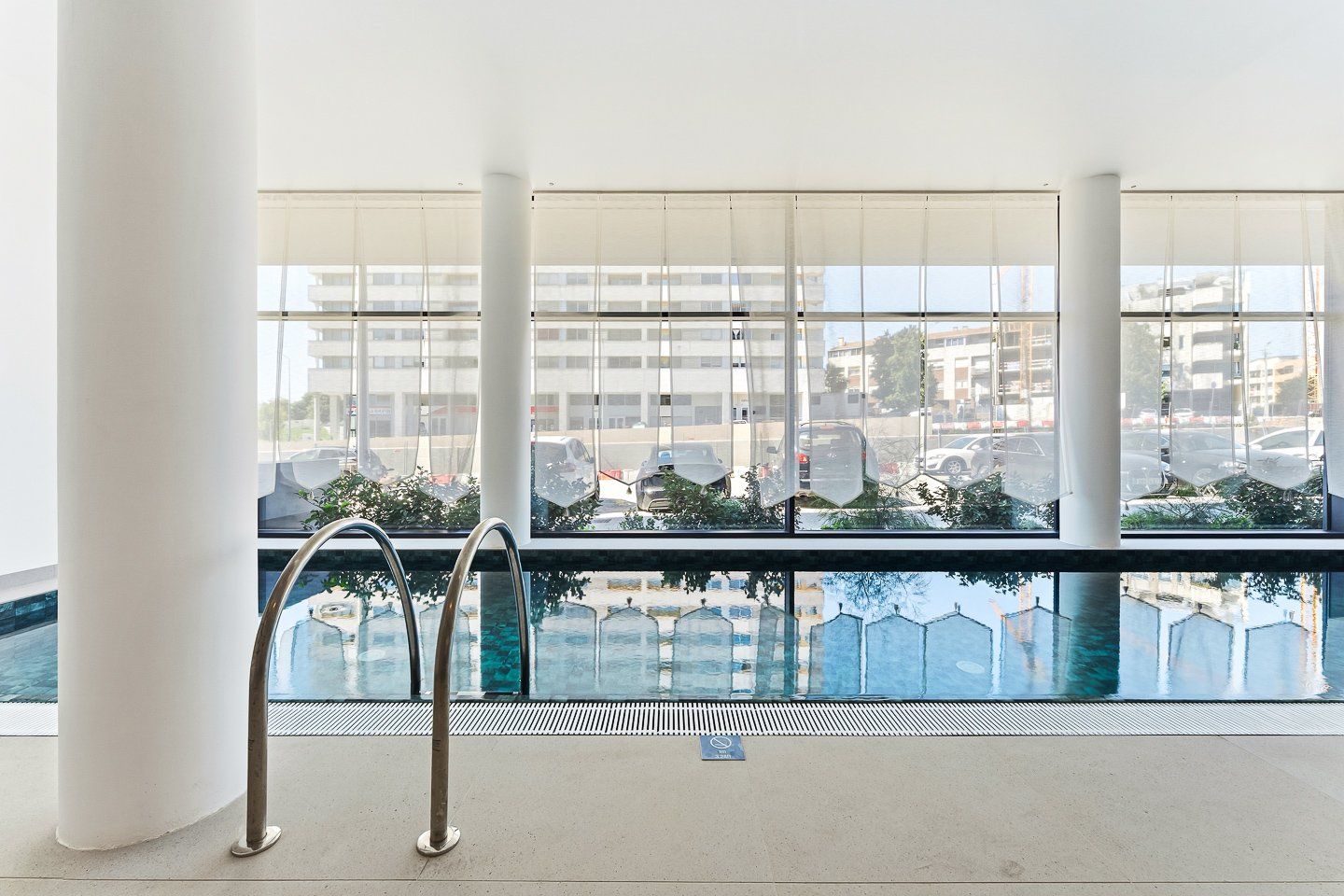 Une piscine avec vue sur les immeubles et les voitures garées, grâce à de grandes fenêtres.