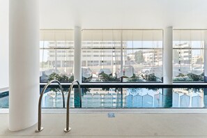 A swimming pool with a view of buildings and parked cars through large windows. - GuestReady - Modern Studio with Balcony & Pool (Vila Nova de Gaia)
