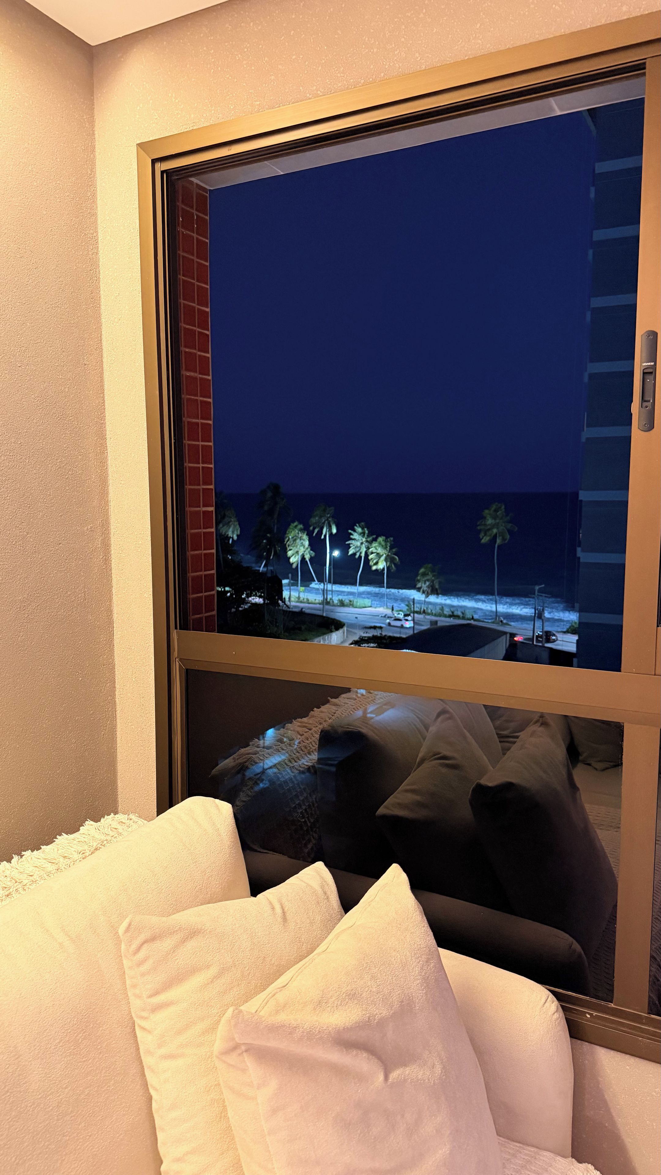 A room with a large window overlooking a beach at night.